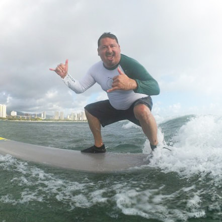 Owner and Instructor, John, of Polu Lani Surf catching a wave throwing a double shaka!