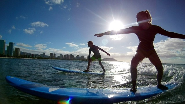 A guy and girl catching the same wave, with the beautiful city skyline as their backdrop. Provided by Polu Lani Surf.
