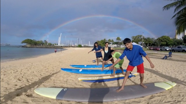 A family of 4 practicing their surf stance on the beach, getting ready for their private surf lesson. Provided by Polu Lani Surf.