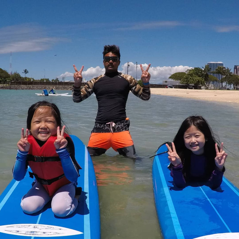 Two young girls and instructors posing from the water, about to start their private surf lesson. Provided by Polu Lani Surf.